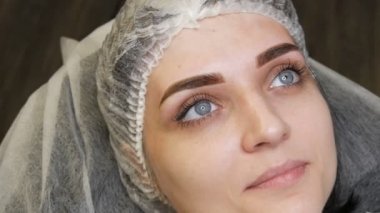 Mavi gözlü ve uzun kirpikli güzel bir kadının yüz portresi. Kalıcı makyajdan sonra kaş dövmeli mikroplar bir kanepede uzanıyor.