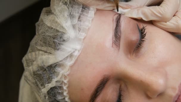 Uma máquina de tatuagem de agulha especial faz a correção de maquiagem permanente de sobrancelhas de mulheres jovens. Um pigmento de tinta escura é injetado sob a pele. Microblading, pulverização em pó — Vídeo de Stock