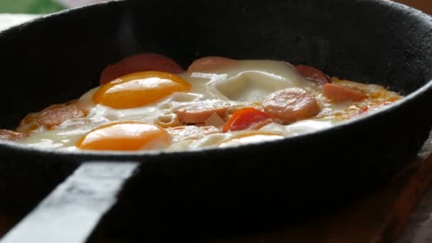 Leckere frische Spiegeleier in einer gusseisernen Pfanne mit Gewürzen, Tomaten, süßem Paprika und Würstchen mit Dampf. Morgens Frühstück, runde Eigelb in der heimischen Küche — Stockvideo