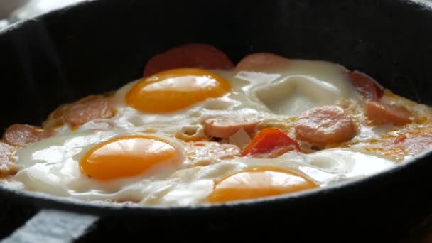 Smaka färska stekta ägg i en gammal stekpanna av gjutjärn, med kryddor, tomater, söt paprika och korv, med ånga. Morgon frukost, runda äggulor i köket — Stockvideo