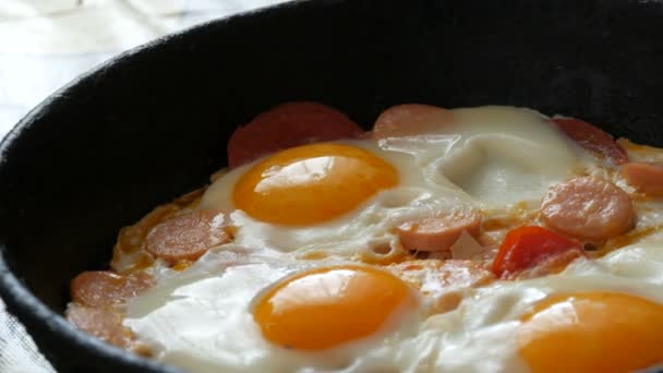 Smaka färska stekta ägg i en gammal stekpanna av gjutjärn, med kryddor, tomater, söt paprika och korv, med ånga. Morgon frukost, runda äggulor i köket — Stockvideo