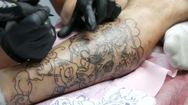 Bir profesyonelin yakından bakınca, salondaki bir adamın bacağına dövme yapıyor. Döner dövmeli makineli tüfekle çizim