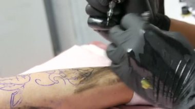 Bir profesyonelin yakından bakınca, salondaki bir adamın bacağına dövme yapıyor. Döner dövmeli makineli tüfekle çizim