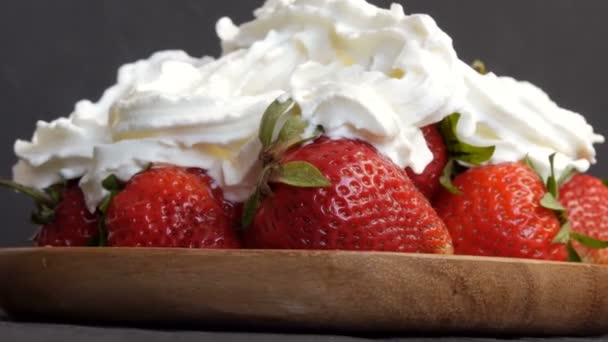 Juicy ripe big red strawberries on an eco bamboo plate on top with whipped cream close up view — Stock Video