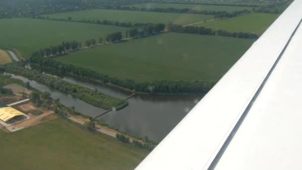 La vue depuis la fenêtre du hublot d'un petit avion de passagers contre une aile blanche. Vue de dessus de la nature, de la rivière et des champs verts sur fond d'aile blanche