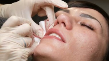 Kozmetoloji kliniğindeki dudak rengini düzelten özel renk pigmentli mikro patenli dudak dövmesi. Eller, dövme makinesiyle dudaklara pigment makyajı uygulayarak kalıcı makyaj yapar.