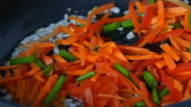 Vejetaryen sağlıklı beslenme. Asya yemekleri. Sebzeler tavada kızartılır. Paprika, havuç, soğan, sarımsak, yeşil kapsüller ahşap mutfak spatulasıyla karıştırılmış.