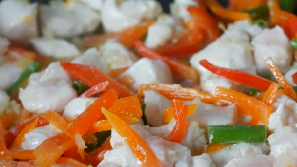 Aziatisch eten. Groenten worden gebakken in een pan met stukjes kip. Paprika, wortelen, uien, knoflook, groene peulen van dichtbij bekijken — Stockvideo