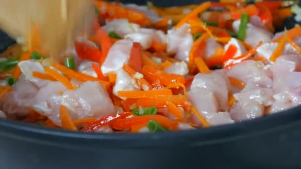 Asijské jídlo. Zelenina se smaží na pánvi s kousky kuřete. Paprika, mrkev, cibule, česnek, zelené lusky smíchané s dřevěnou kuchyňskou špachtlí a dušené — Stock video