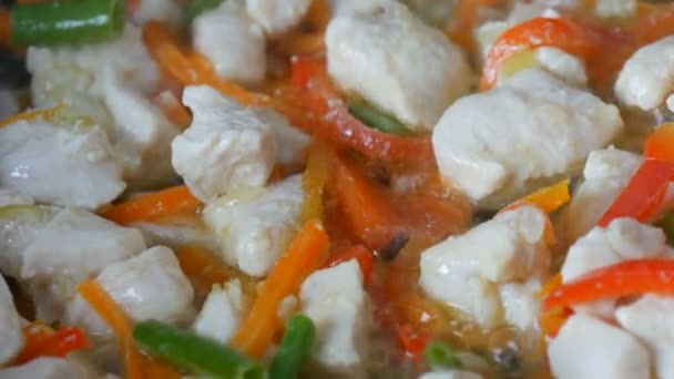 Asian food. Vegetables are fried in a pan with pieces of chicken. Paprika, carrots, onions, garlic, green pods close up view — Stock Video