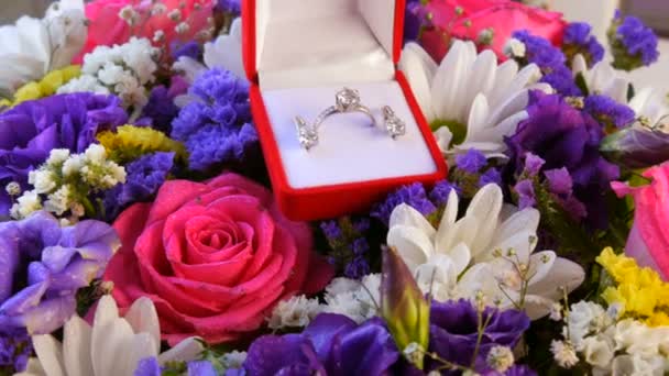 Geschenk Geschenk-Geschenk rote Box mit einem Satz Verlobungsring und Ohrringe auf dem Hintergrund eines bunten schönen Blumenstrauß. Heiratsantrag. Weißgold oder Silber mit Diamantstein. — Stockvideo