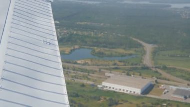 Bir yolcu uçağının beyaz kanadı, güzel mavi bir gölün doğa manzarasına karşı, bir göletin üzerinde uçar, yeşil ormanlar ve küçük evler ve kasabalar. Seyahat kavramı