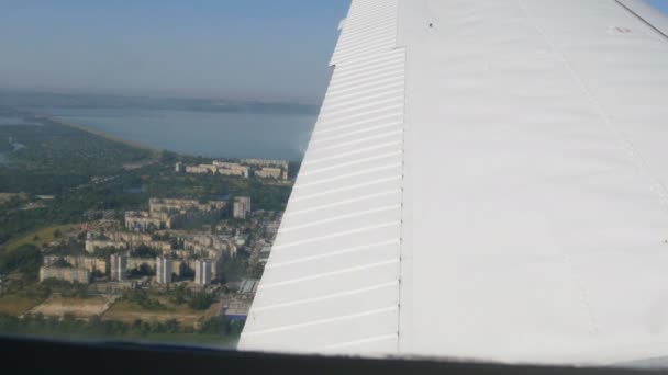 Witte vleugel van een passagiersvliegtuig tegen de achtergrond van een grote woonwijk, meerdere verdiepingen tellende gebouwen vanuit het raam van het vliegtuig bovenaanzicht — Stockvideo