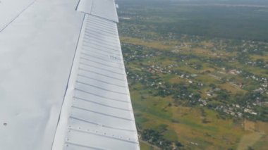 Küçük bir yolcu uçağının penceresinden beyaz bir kanada bakan manzara. Beyaz bir kanadın arka planına karşı doğa, nehir ve yeşil alanların üst görünümü