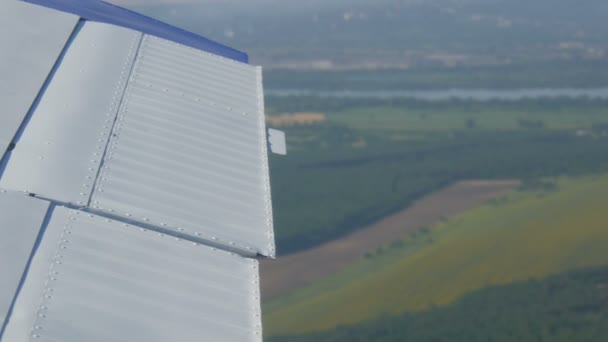 A vista da janela do pórtico de um pequeno avião de passageiros contra uma asa branca. Vista superior da natureza, rio e campos verdes contra o fundo de uma asa branca — Vídeo de Stock