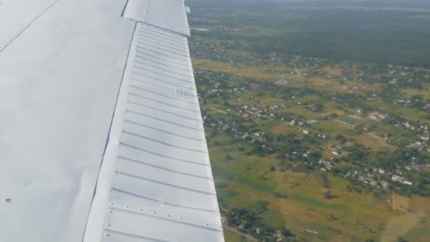 Widok z okna otworu małego samolotu pasażerskiego na białe skrzydło. Górny widok na przyrodę, rzekę i zielone pola na tle białego skrzydła — Wideo stockowe