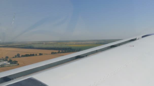 Вид из окна иллюминатора маленького пассажирского самолета на белое крыло. Вид сверху на природу, реку и зеленые поля на фоне белого крыла — стоковое видео