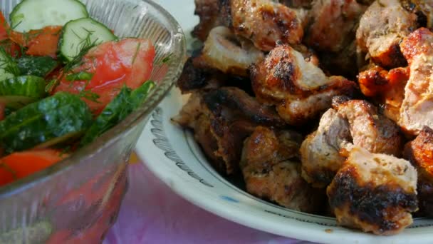 Fresh vegetarian salad of cucumber tomatoes and greens in a large salad bowl next to grilled pieces of pork meat — Stock Video