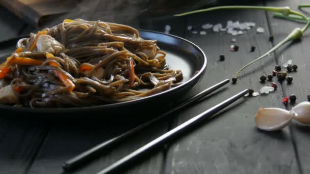 蒸したてのアジアそばのそばに野菜のタマネギの鞘、人参、パプリカ、鶏肉を盛り付け、おしゃれな黒プレートと中華箸で。 — ストック動画