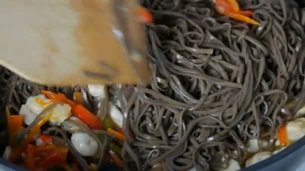 Het koken van Aziatische boekweit noedels soba met groenten ui peulen, wortelen, paprika en stukjes kip in grote noodle pan. Roeren met een keukenspatel — Stockvideo