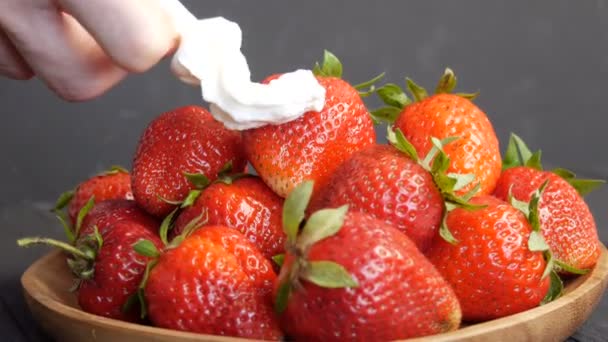 Fresas rojas grandes maduras jugosas en un plato de bambú ecológico en la parte superior con crema batida con una mano femenina — Vídeos de Stock