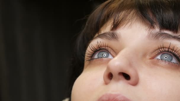 El retrato de la cara de una hermosa joven con ojos azules y pestañas largas antes del procedimiento de maquillaje permanente por microblading con tatuaje de cejas se encuentra en un sofá en un salón de belleza — Vídeo de stock
