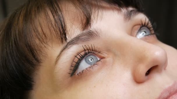 Ansiktsporträtt av en vacker ung kvinna med blå ögon och långa ögonfransar innan förfarandet för permanent make up genom microblading med ögonbrynstatuering ligger på en soffa i en skönhetssalong — Stockvideo