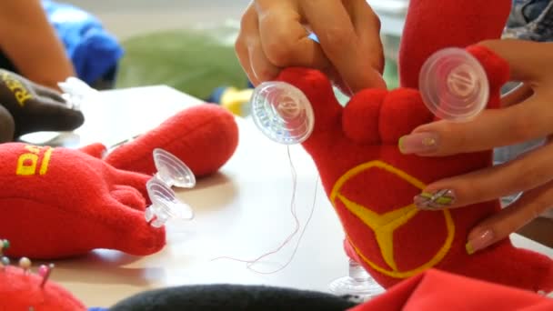 Kamenskoe, Ucrânia - 20 de julho de 2020: Fábrica para a produção de brinquedos leves para crianças. Uma mão de mulher cose um rabo a um brinquedo vermelho com uma agulha e fio em uma oficina de costura — Vídeo de Stock