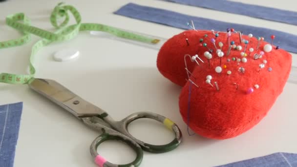 Kit da cucire, forbici da cucire, scarti di tessuto blu, un cuscino rosso con aghi a forma di cuore, un centimetro su uno sfondo bianco del tavolo. Laboratorio di cucito, flusso di lavoro della fabbrica del giocattolo — Video Stock