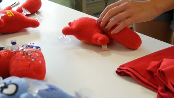 Kamenskoe,ウクライナ- 2020年7月20日:子供の柔らかいおもちゃの生産のための工場.女性の手は針と糸で赤いおもちゃに尾を縫いつける。 — ストック動画