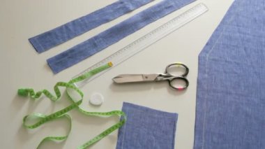 Dikiş takımı, makas, mavi kumaş paçavraları, beyaz masa arkasında santimetre. Dikiş atölyesi, oyuncak fabrikası iş akışı