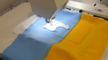 Nakış işlemek için kullanılan dikiş makinesinin iğnesi mavi ve sarı bir kumaş parçasına bir süs yapar. İşyerinde nakış işlemek için özel dikiş makinesi. Programlanabilir dikiş makinesi