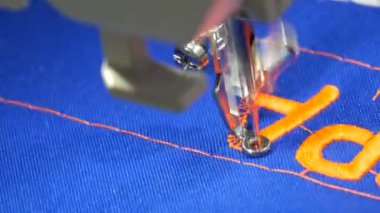 Dikiş makinesinden özel bir iğne. Terzi dükkanındaki mavi kumaşa turuncu harfler nakışlıyor. Ya da dikim atölyesini kapatıyor.