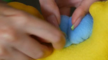 Sarı bir oyuncağın üzerine manikür dikilmiş bir terzinin kadın elleri. Dikiş atölyesi, oyuncak fabrikası