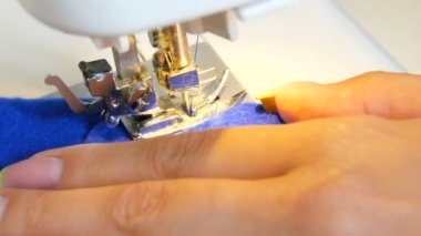 Genç kadın el terzisi dikiş makinesine dikiş dikiyor. Dikiş makinesinin iğne ve ayağı kumaşa dikiş atar.