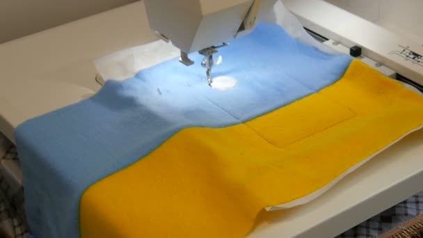 Nakış işlemek için kullanılan dikiş makinesinin iğnesi mavi ve sarı bir kumaş parçasına bir süs yapar. İşyerinde nakış işlemek için özel dikiş makinesi. Programlanabilir dikiş makinesi — Stok video