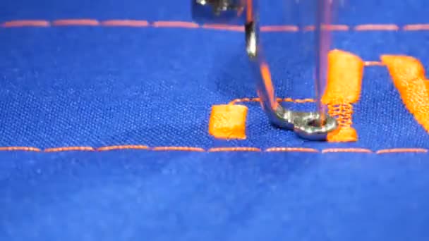 Спеціальна голка зі швейної машинки вишиває помаранчеві літери на синій тканині в крамниці-вишивальниці або в майстерні з шиття крупним планом — стокове відео