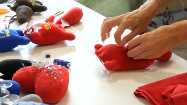 Kamenskoe, Ukraina - 20 lipca 2020: Fabryka do produkcji dziecięcych zabawek miękkich. Ręka kobiety przyszywa ogon do czerwonej zabawki igłą i nitką w warsztacie szycia — Wideo stockowe
