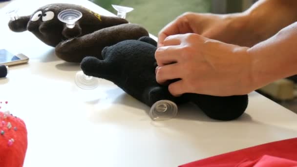Kamenskoe, Ucrânia - 20 de julho de 2020: Fábrica para a produção de brinquedos leves para crianças. Uma mão de mulher cose um rabo a um brinquedo preto com uma agulha e fio em uma oficina de costura — Vídeo de Stock