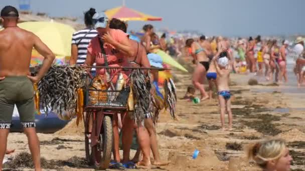 Schastlivtsevo, Ucrania - 2 de agosto de 2020: Muchas personas en la playa, descansando en el Mar de Azov. El vendedor de un gran paquete de paseos de pescado seco y vende en la playa — Vídeos de Stock