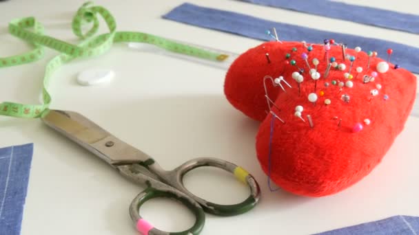 Kit de costura, tijeras de coser, trozos de tela azul, un cojín de alfiler rojo con agujas en forma de corazón, un centímetro sobre un fondo de mesa blanco. Taller de costura, flujo de trabajo de fábrica de juguetes — Vídeos de Stock