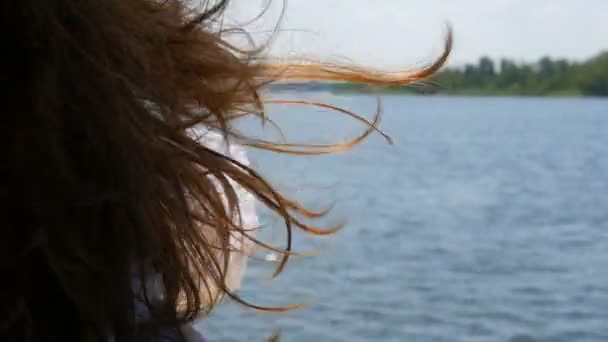 Bellissimi lunghi capelli scuri di una giovane ragazza ondeggia nel vento sullo sfondo di una gita in barca in estate, l'acqua limpida blu brilla e riflette la luce del sole. Relax concept, riposo — Video Stock