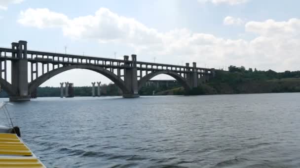 Zaporizhzhia, Ucrania - 19 de junio de 2020: barco de recreo turístico navega bajo un gran puente de hormigón viejo cerca de la vista. — Vídeo de stock