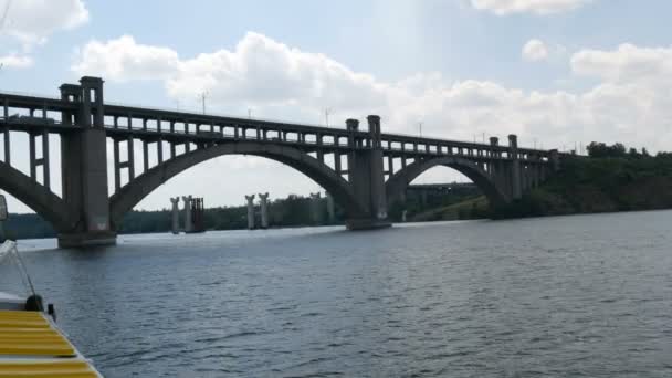 Saporizhzhia, Ukraine - 19. Juni 2020: Touristisches Ausflugsboot segelt unter einer großen alten Betonbrücke in Sichtweite. — Stockvideo