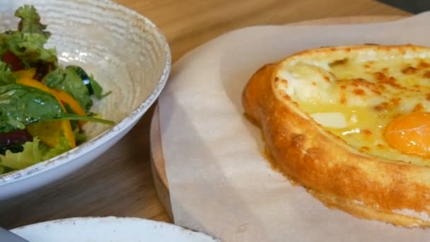 Delicioso georgiano Adjarian khachapuri no restaurante georgiano, cozinha autêntica nacional. Salada vegetariana de verduras e verduras de tomates, páprica, pepinos de alface, servido em um prato elegante — Vídeo de Stock