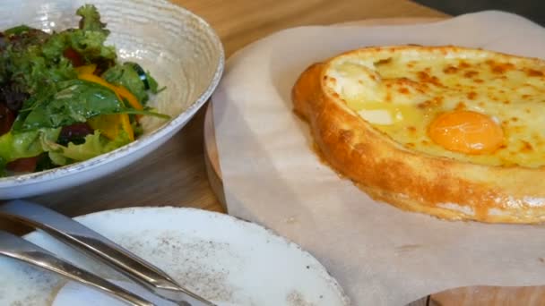 Lahodné gruzínské adjarian khachapuri v gruzínské restauraci, národní autentické kuchyně. Vegetariánský salát ze zeleniny a rajčat, papriky, salátových okurek, podávaný na stylovém pokrmu — Stock video