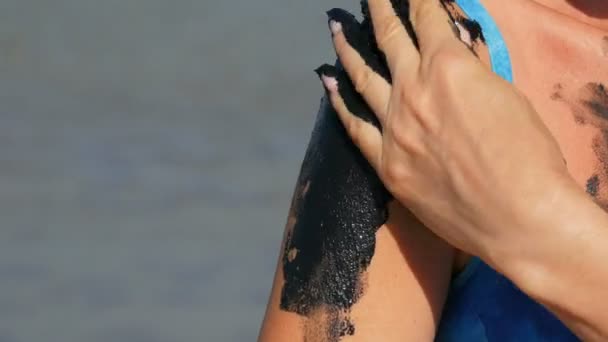 Curación de barro médico negro se aplica a la mujer del brazo en el lago de agua salada. Suciedad negra salada para personas con problemas de salud y piel. Relájese en el spa. Tratamiento de belleza exfoliación exfoliación exfoliación — Vídeos de Stock