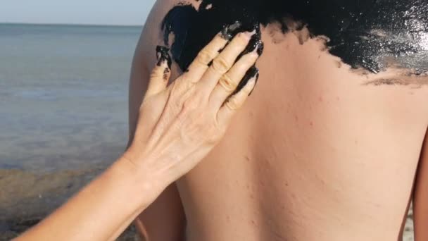 Mam smeert geneeskrachtige modder op tienerzoon bij het meer van zout water. Zout zwart vuil is goed voor mensen met gezondheids- en huidproblemen. Ontspan in het kuuroord. Exfoliatie scrub schoonheidsbehandeling — Stockvideo