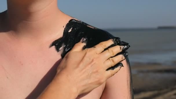 Máma ruka šmouhy léčivé bahno na dospívající syn ramena u jezera slané vody. Slaná černá hlína je dobrá pro lidi se zdravotními a kožními problémy. Odpočiňte si v lázních. Exfoliation scrub beauty treatment — Stock video