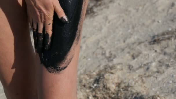 Healing black medical mud applies to leg and knee woman at the lake of salt water. Salty black dirt for people with health and skin problems. Relax at spa resort. Exfoliation scrub beauty treatment — Stock Video